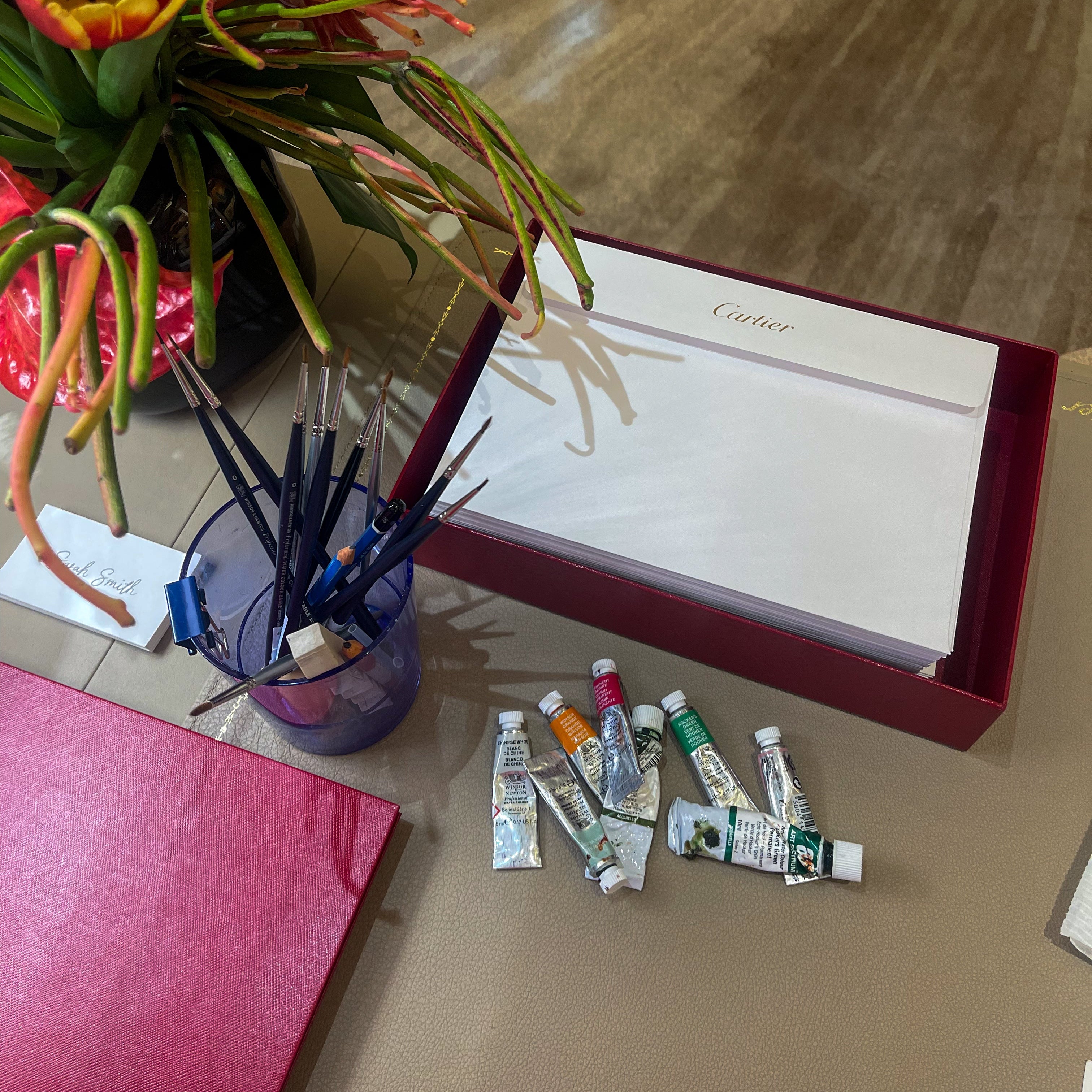 Art supplies including paint tubes, brushes, and a Cacharel product on a wooden surface.